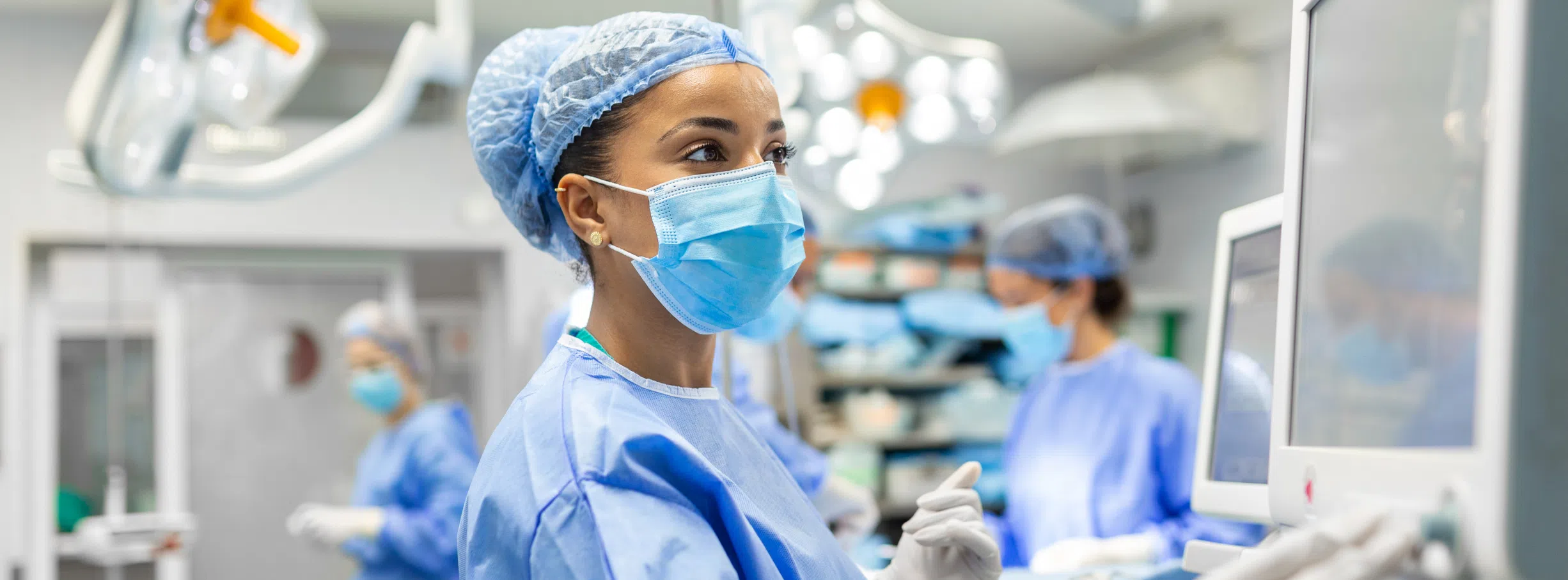 A young female doctor reviews the computer screen mid-operation in the Operating Room.